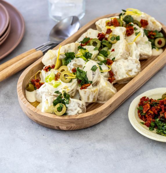 Bowl of potato salad with olives and sun-dried tomato topping.
