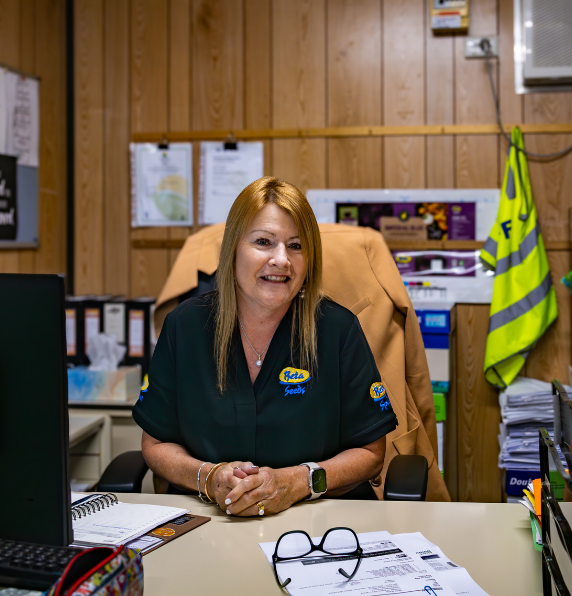Denise Murray from Beta Spuds smiling while sitting at her office desk with her hands clasped.